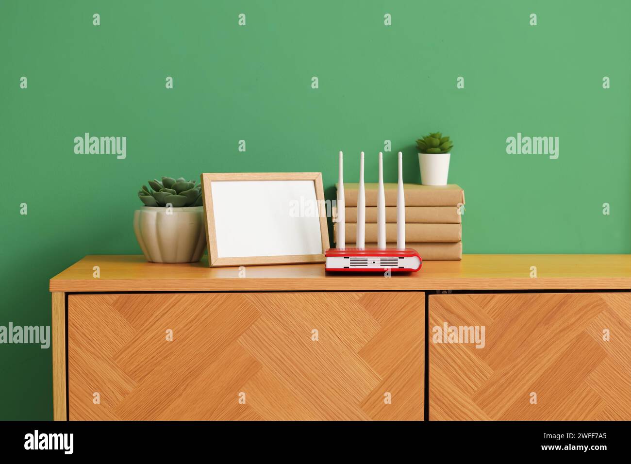 Modern Wi-fi Router With Books, Blank Frame And Plants On Commode Near 