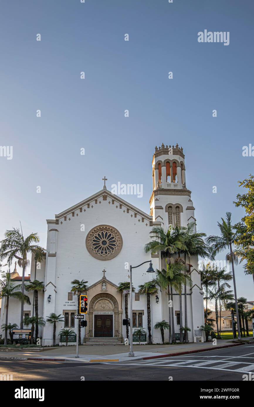 Santa Barbara, CA, USA - January 19, 2024: Full frontal, Our Lady of Sorrows church. Sculpted arch around brown wood, set in white wall with rosas on Stock Photo