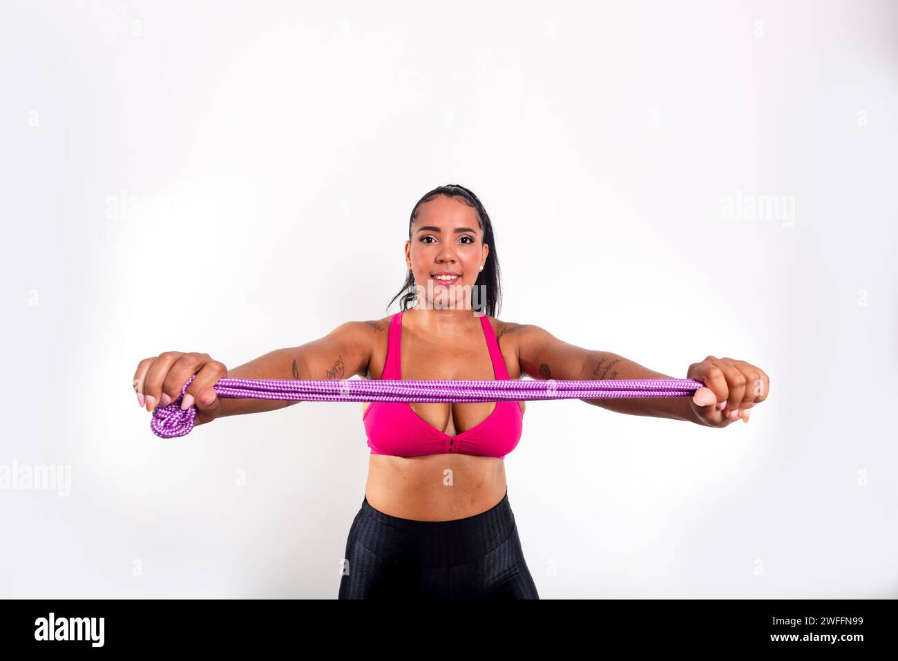 Young gymnast woman holding lilac colored rope for stretching. Against white background. Olympic athlete. Stock Photo