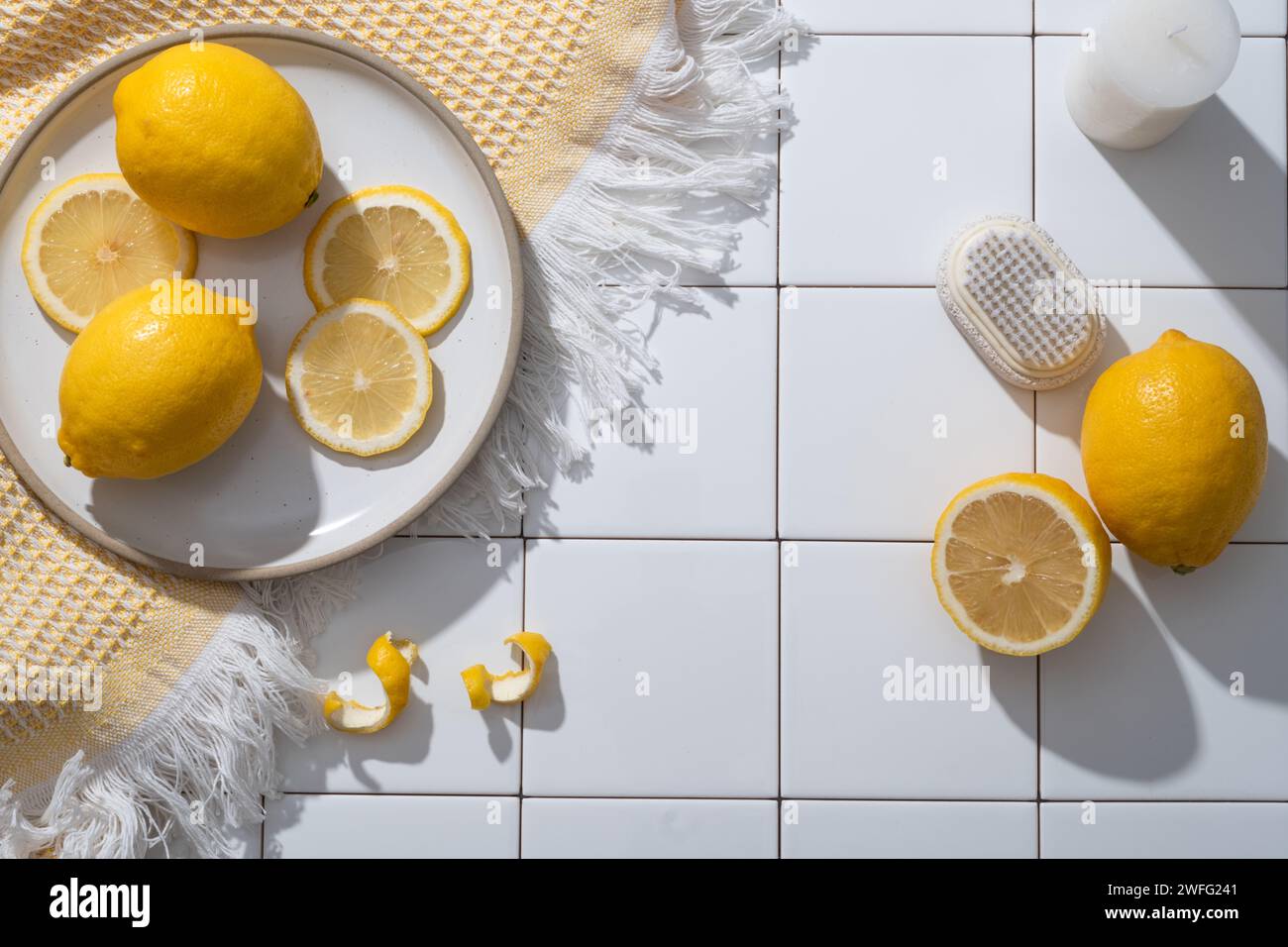 A dish of Lemon slices placed on a wool scarf decorated with candle and a scrub brush. Blank space for product presentation. Copy space. The benefits Stock Photo