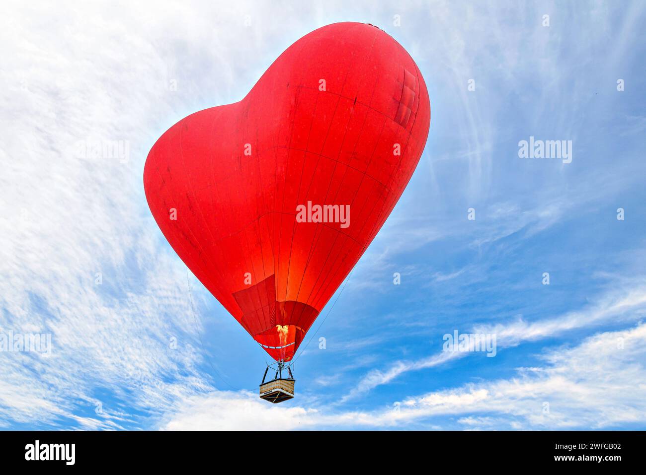 Red heart-shaped hot air balloon flying over a blue sky with white ...