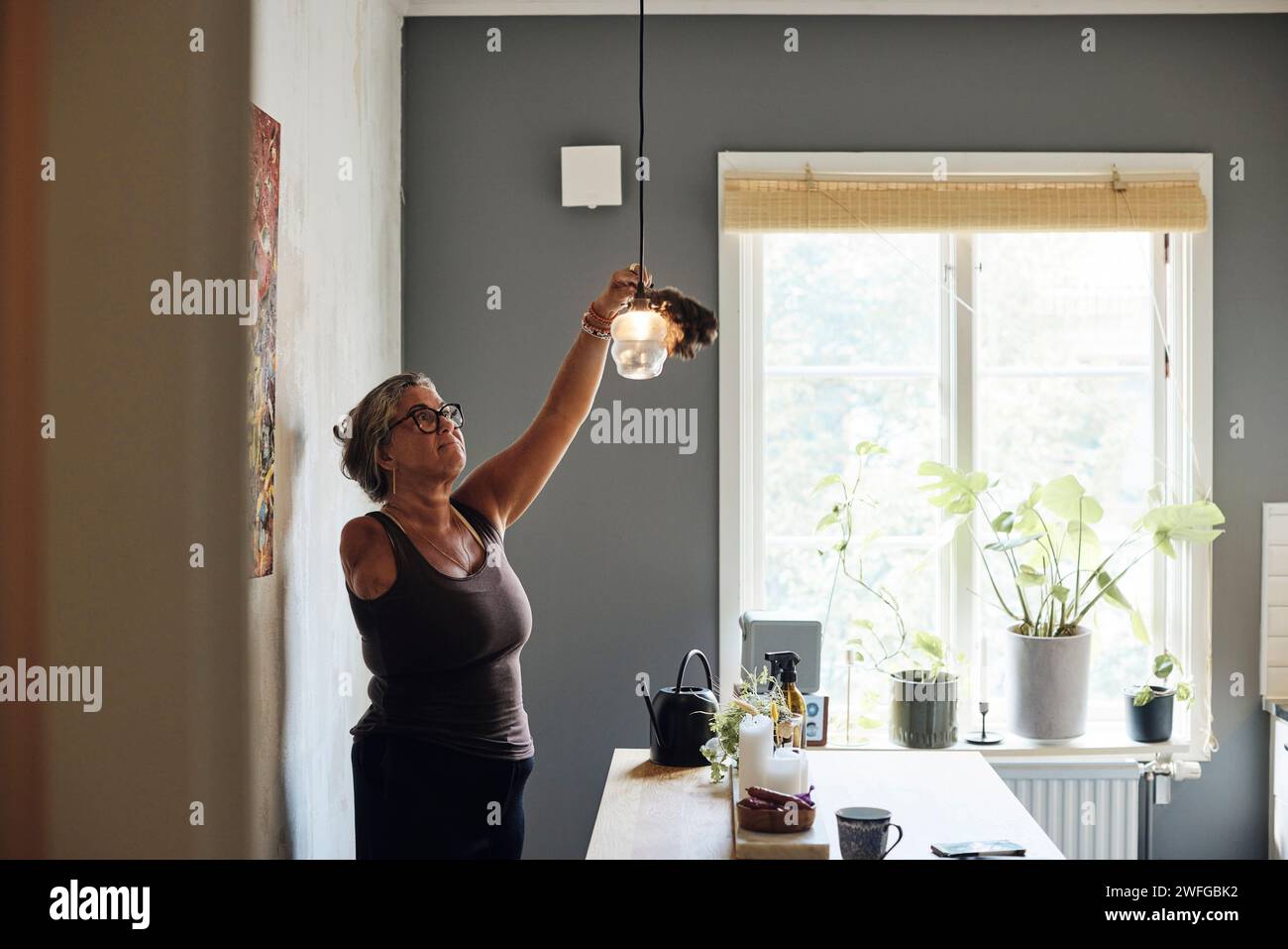 Mature woman with disability cleaning light while standing at home Stock Photo