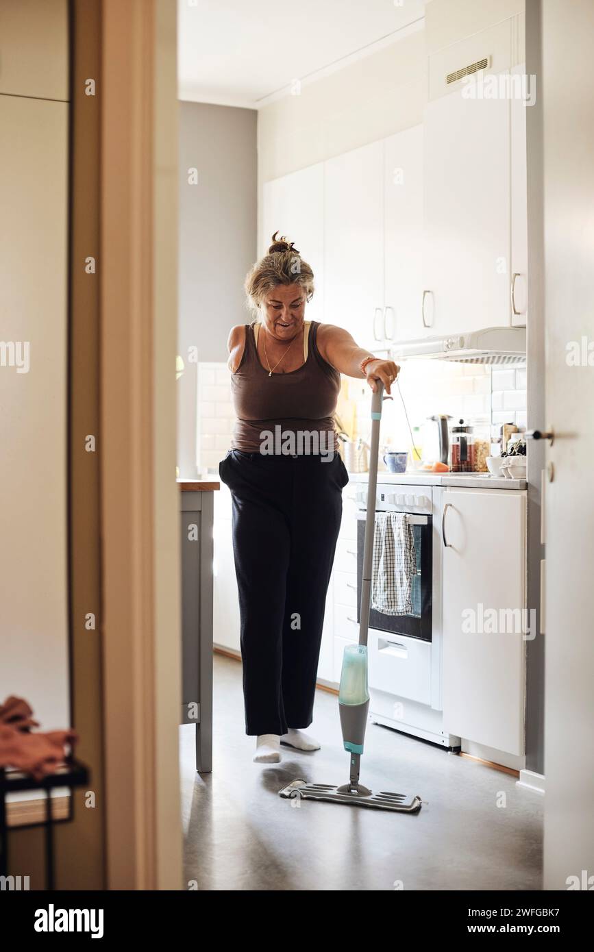 Mature woman with disability mopping kitchen floor at home Stock Photo