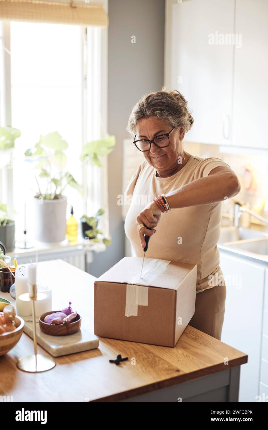 Woman with disability opening package using knife while standing in kitchen at home Stock Photo