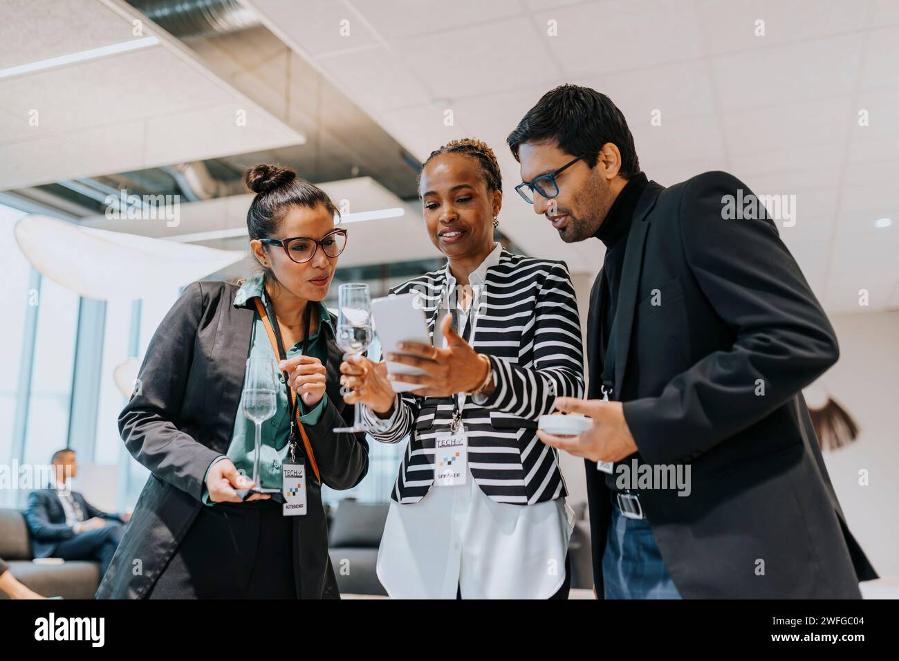 Businesswoman sharing smart phone with delegates during networking seminar Stock Photo