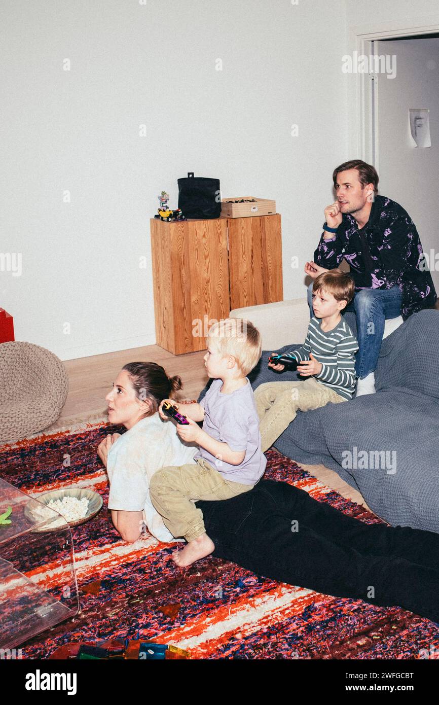 Kids playing video game while sitting with parents at home Stock Photo