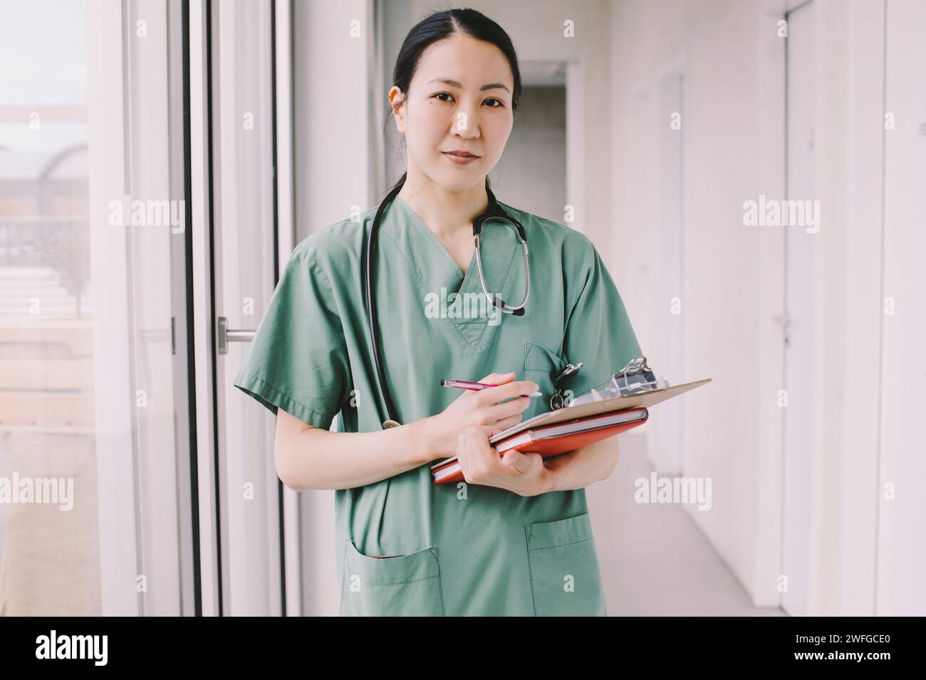 Portrait of confident female physician holding clipboard while standing in hospital corridor Stock Photo