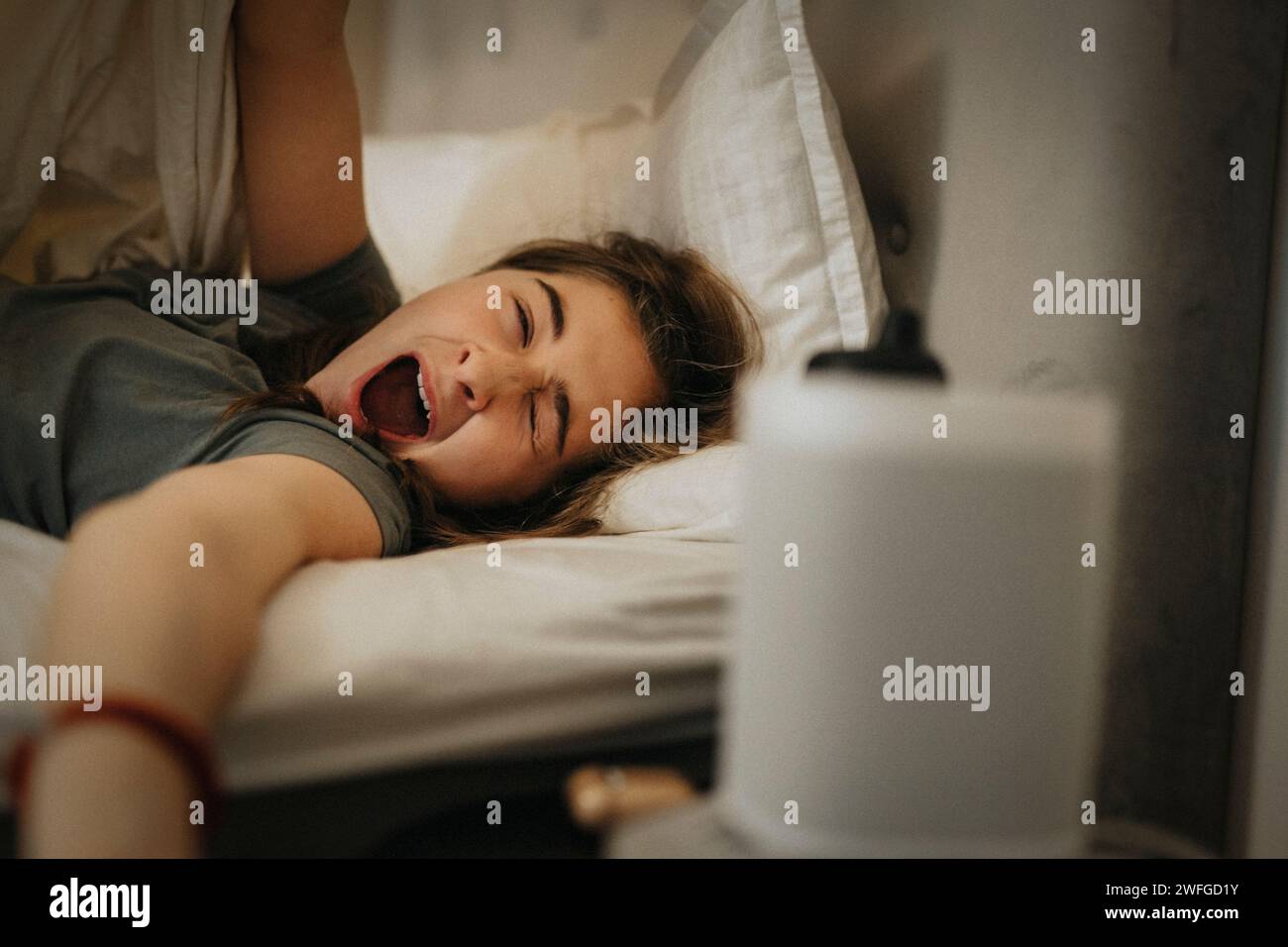 Girl yawning on bed while waking up in morning at home Stock Photo