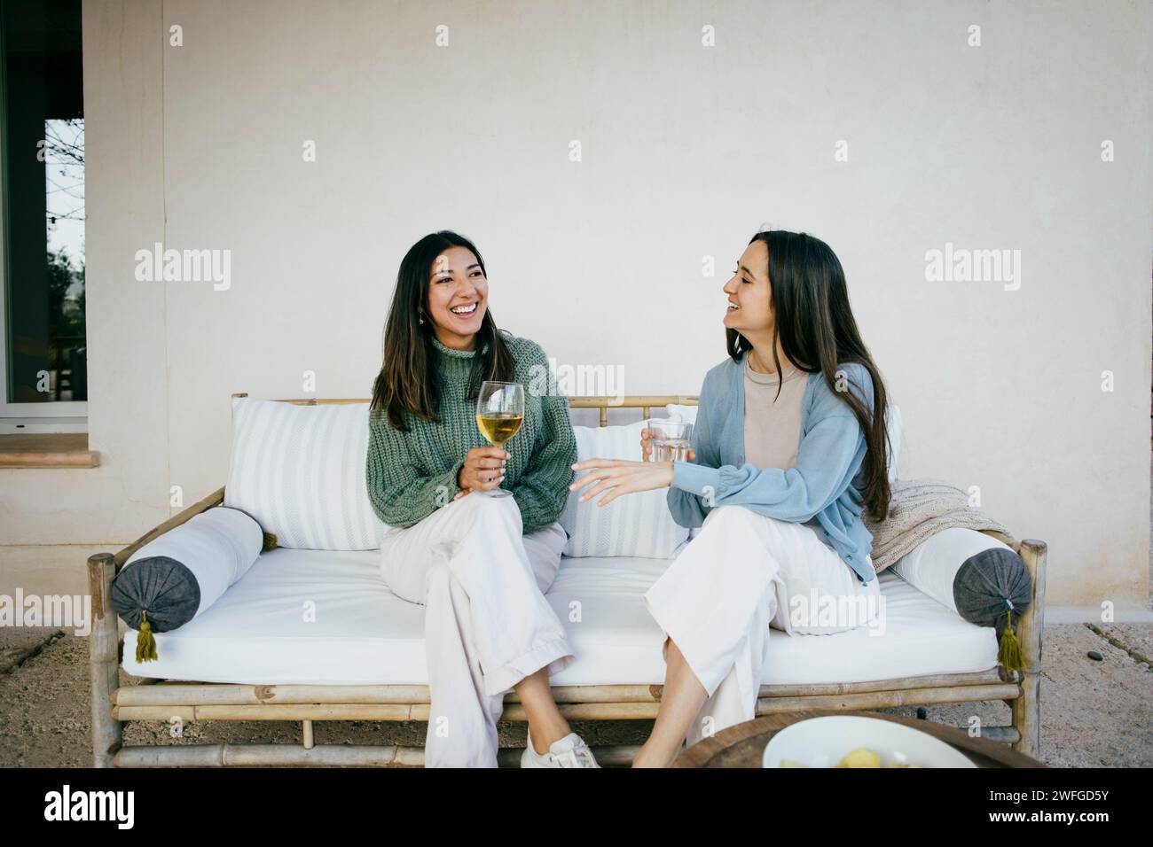 Happy female friends talking while sitting with drinks in backyard Stock Photo