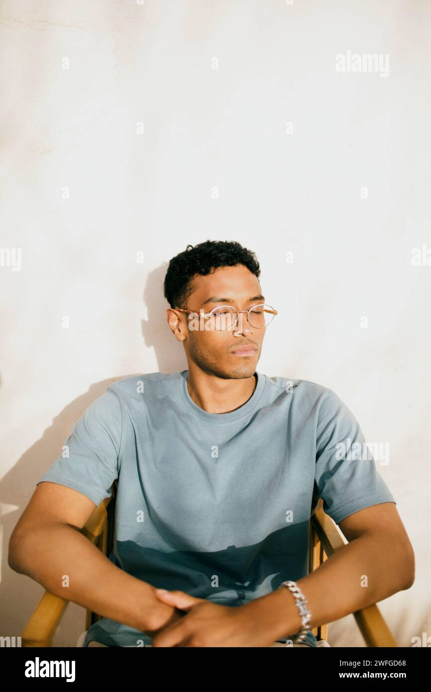 Young man with eyes closed sitting on chair under sunlight at backyard Stock Photo