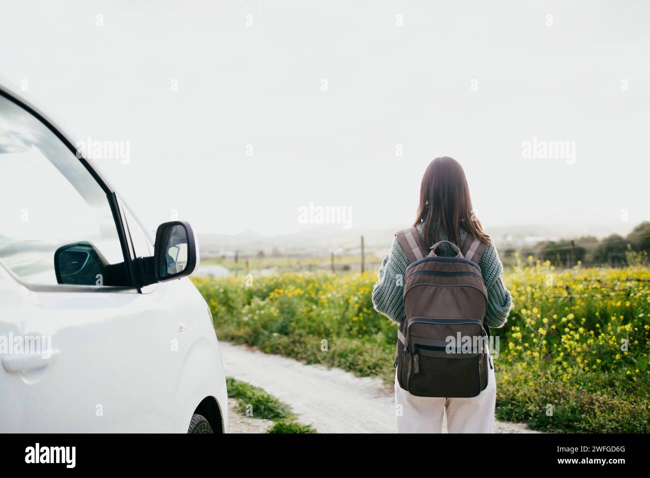Rear view of woman with backpack looking at field standing by van against sky Stock Photo