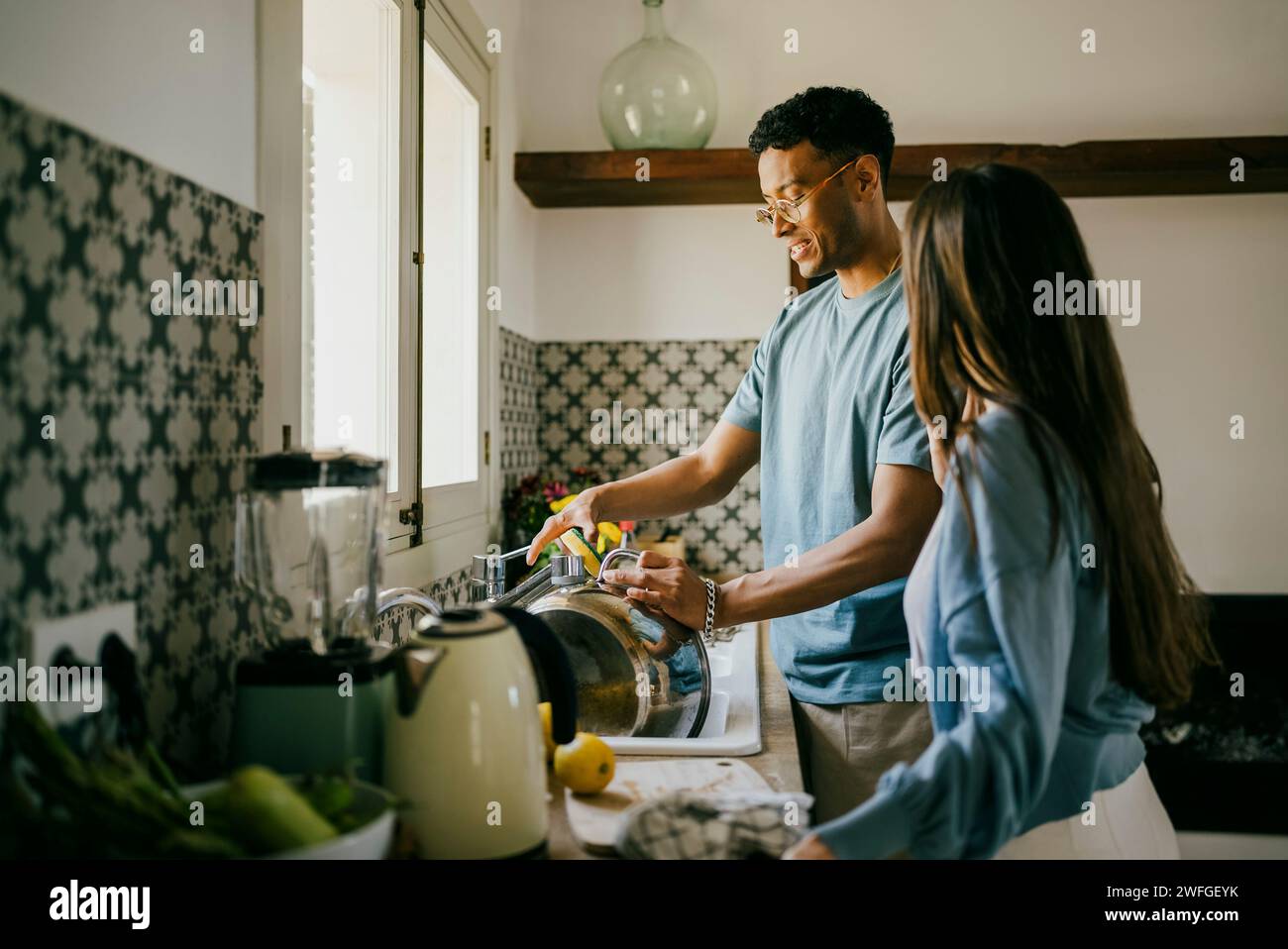 Young man and woman washing dishes together in kitchen sink at home Stock Photo