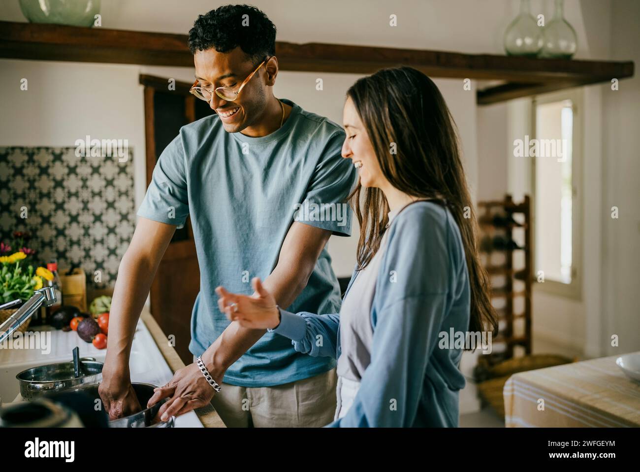 Happy young man and woman washing dishes together in kitchen sink at home Stock Photo