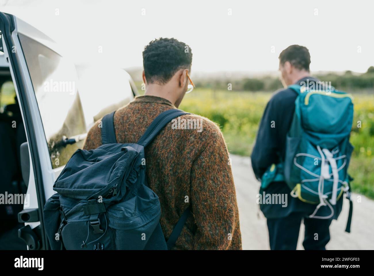 Rear view of male friends with backpacks walking by van Stock Photo