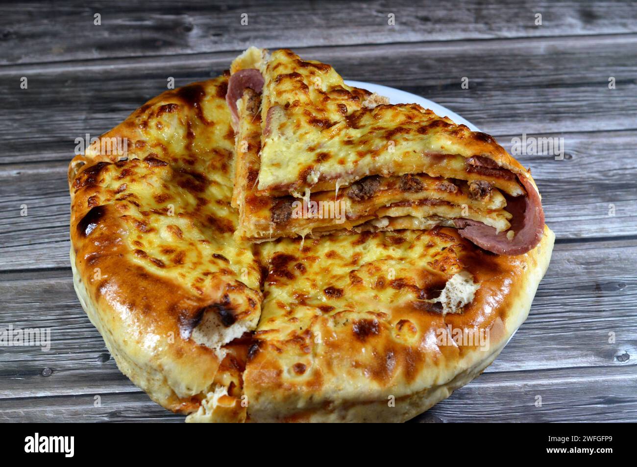 Multi-layers baked pizza cake, consists of layers of salami, barbeque chicken, cheese mix, beef, sausage, mozzarella cheese, baked in the oven, Italia Stock Photo