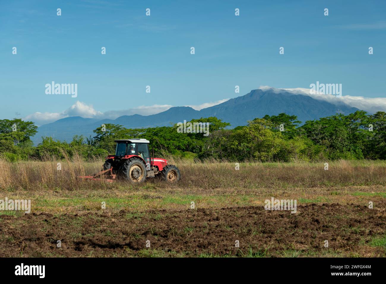 Blue sky over tractor plowing a field with Baru volcano in the ...