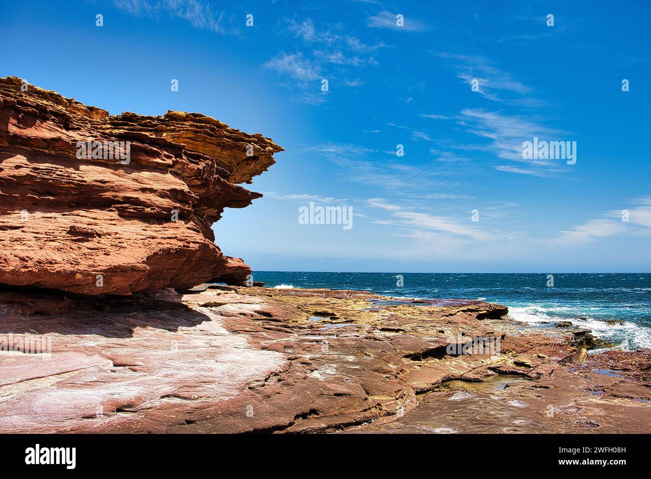 Heavily eroded red-brown sandstone cliffs and rock plateau with rock pools at the coast of Kalbarri National Park, Western Australia. Stock Photo