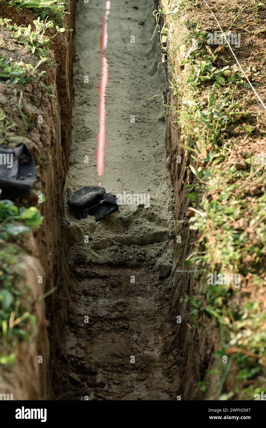 An orange reinforced sewer pipe is compacted with sand in a trench. Plumbing works on a private plot. Stock Photo