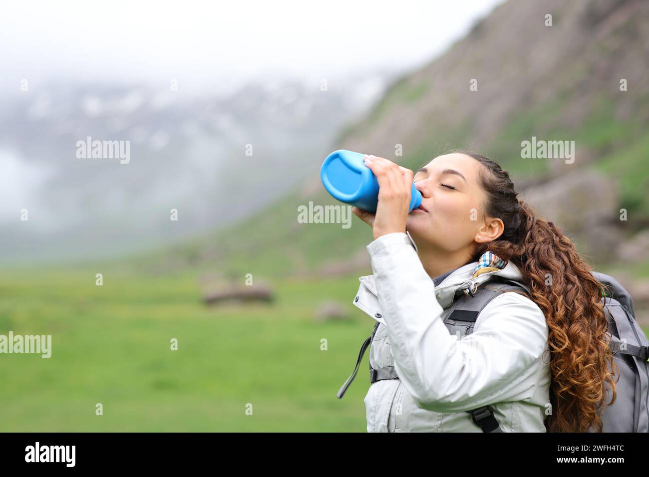 Hiker drinking water from canteen standing in nature Stock Photo