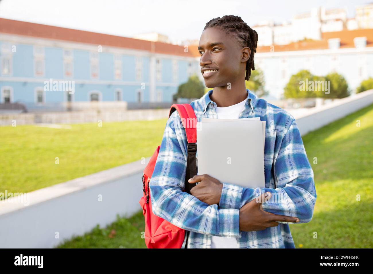 Black student guy hugs laptop standing with backpack near university Stock Photo