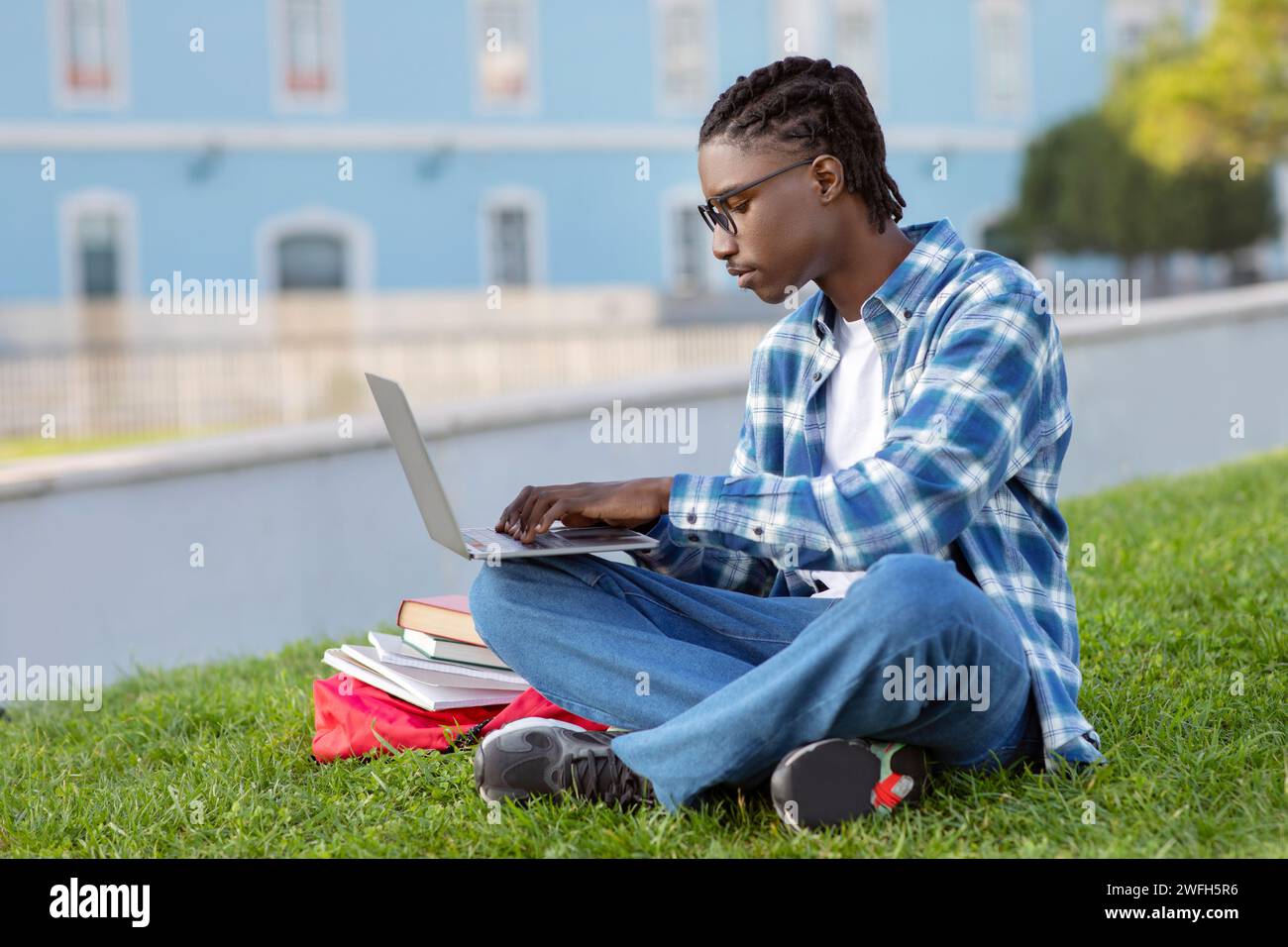 Focused black guy engages in e-learning on his laptop outdoor Stock Photo
