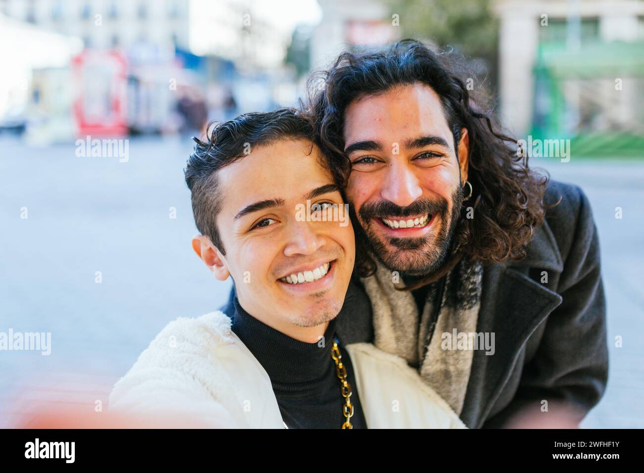 Happy gay couple smiling while taking selfies together outdoors. Stock Photo
