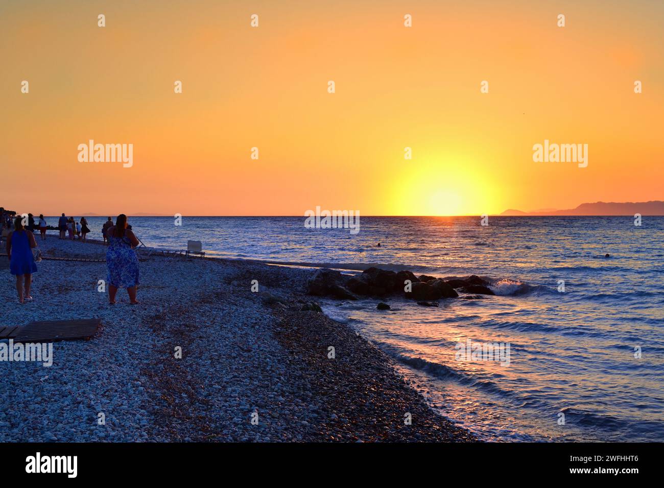 Tourists during sunset time at the beach of Ialyssos in the Greek Island of Rhodes Stock Photo