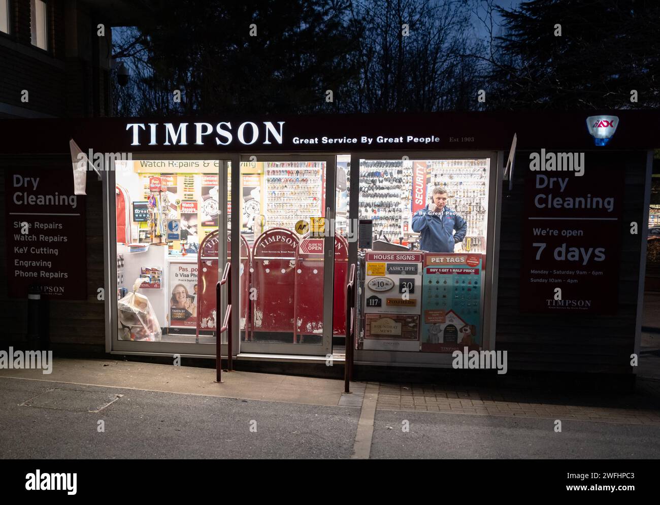 Torquay. Timpson shoes and watch repair and key cutting shop with the cobbler inside on the phone. Night time photograph with shop lit up in the dark. Stock Photo
