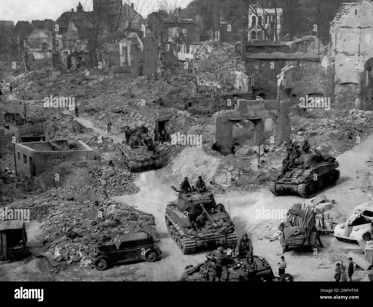 Watched by young children, American tanks and troops patrol the devestated city streets of Nuremberg on the 20th April 1945, during the final days of the Second World War. Stock Photo