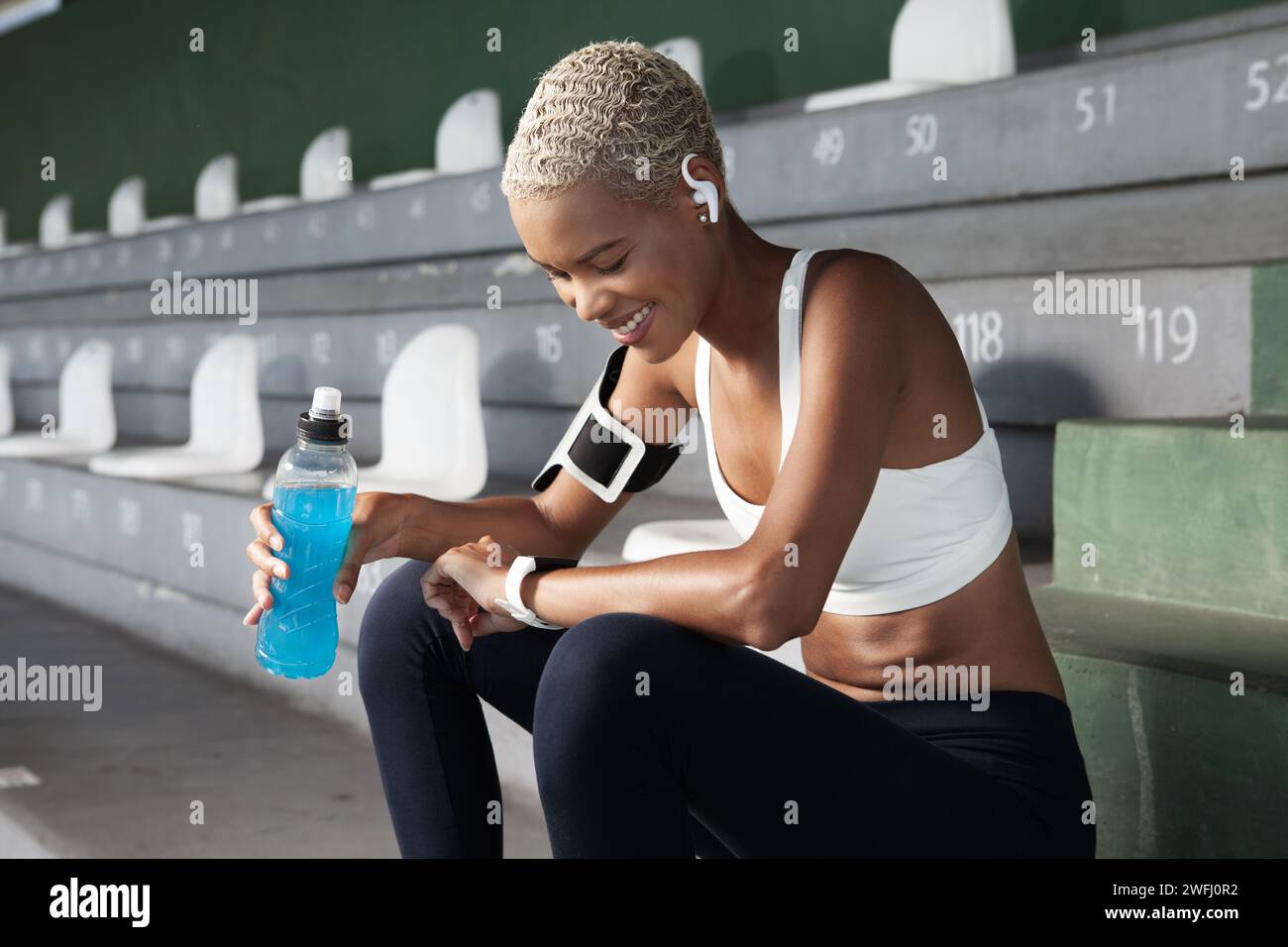 Smiling female athlete drinking energy drink from bottle after running
