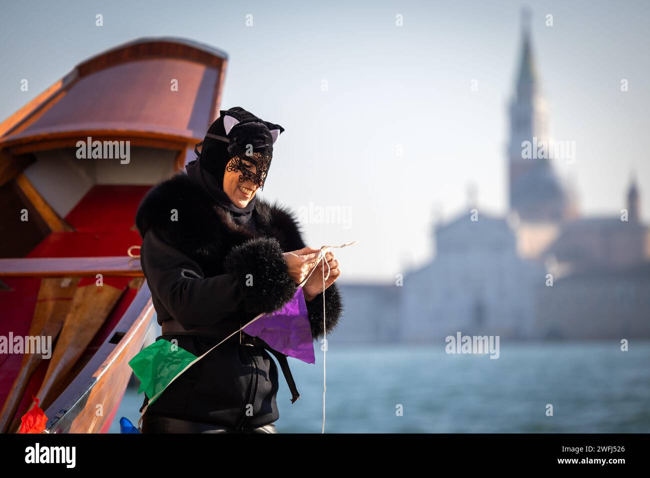 Venice, Veneto, Italy - January 28, 2024: Woman in Carnival Mask Costume Helping With Decorations on Participants Boats of Venetian Carnival Opening R Stock Photo