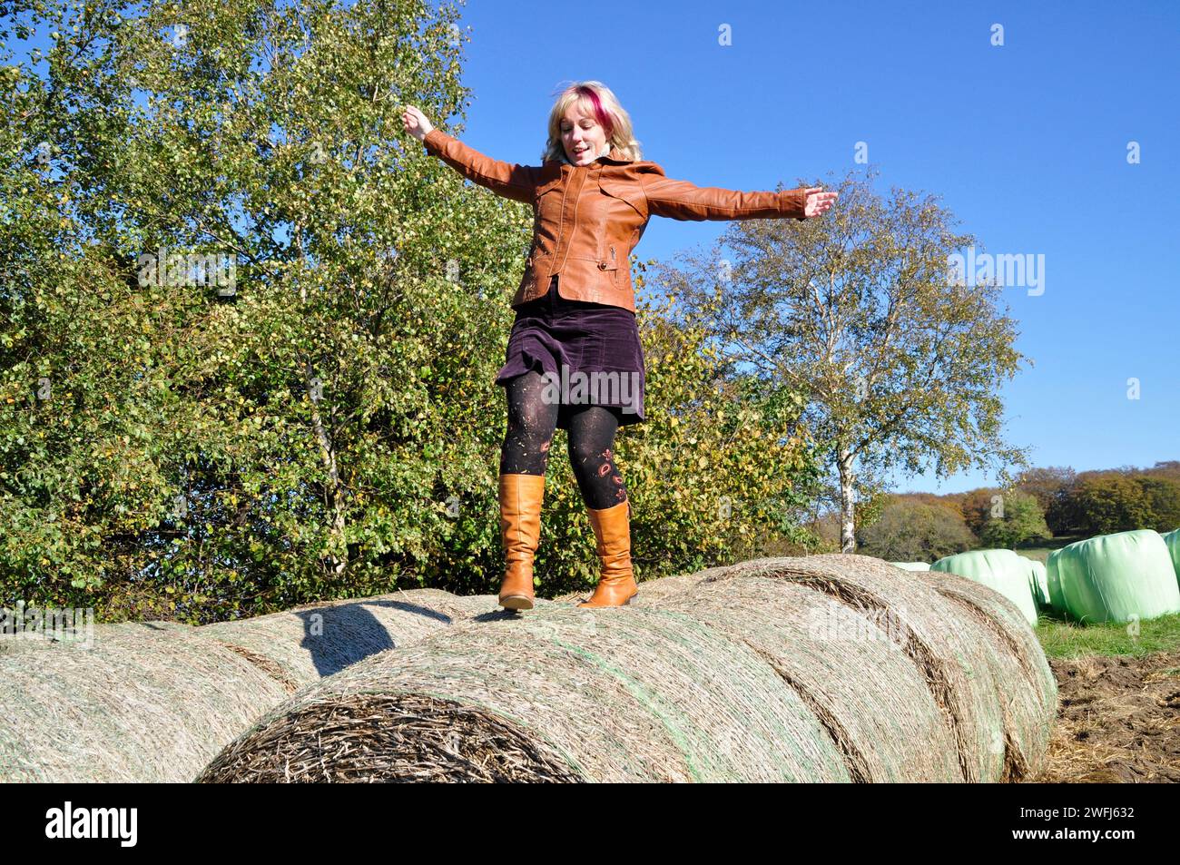 A blonde woman climbs onto silo bales in the fall. Brilon, Germany Stock Photo