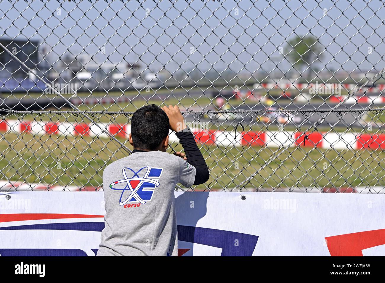 Young pilot leaning on the net and watching race tests at the Go-karting circuit Stock Photo