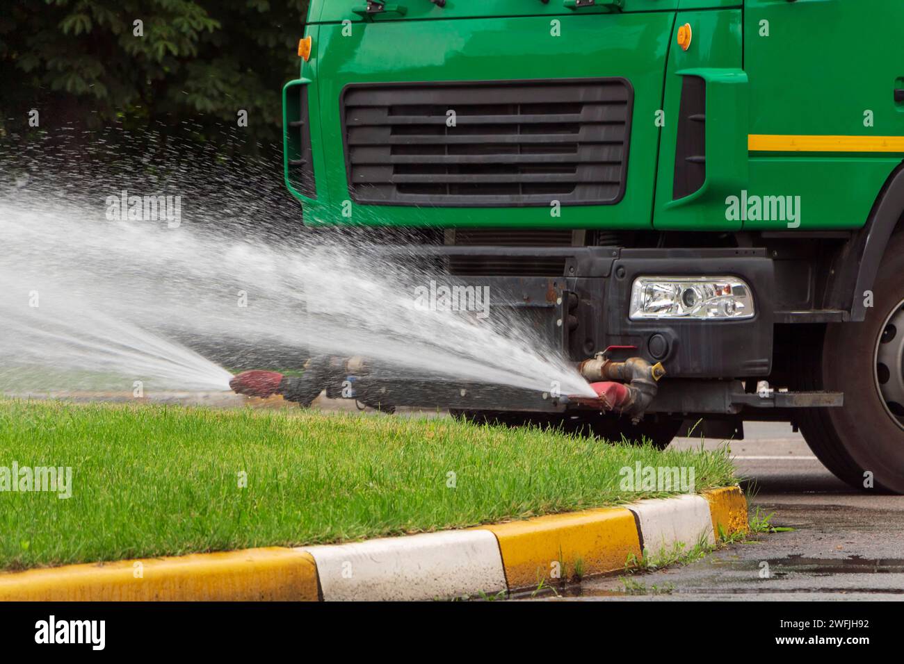 Close up of truck sprinkles water on the green grass. City care services. Stock Photo