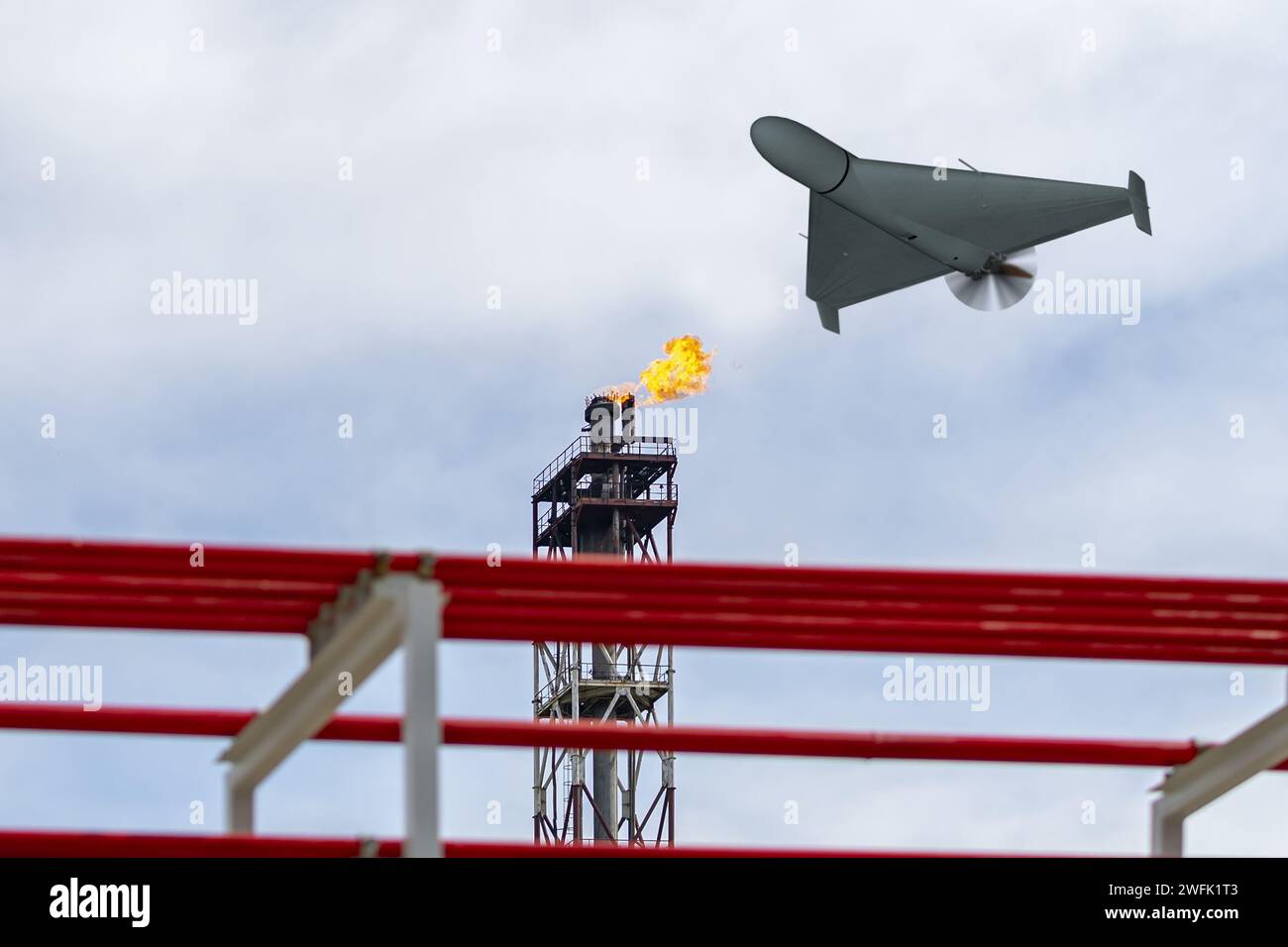 A military drone flies over an oil refinery, fire burning. Stock Photo