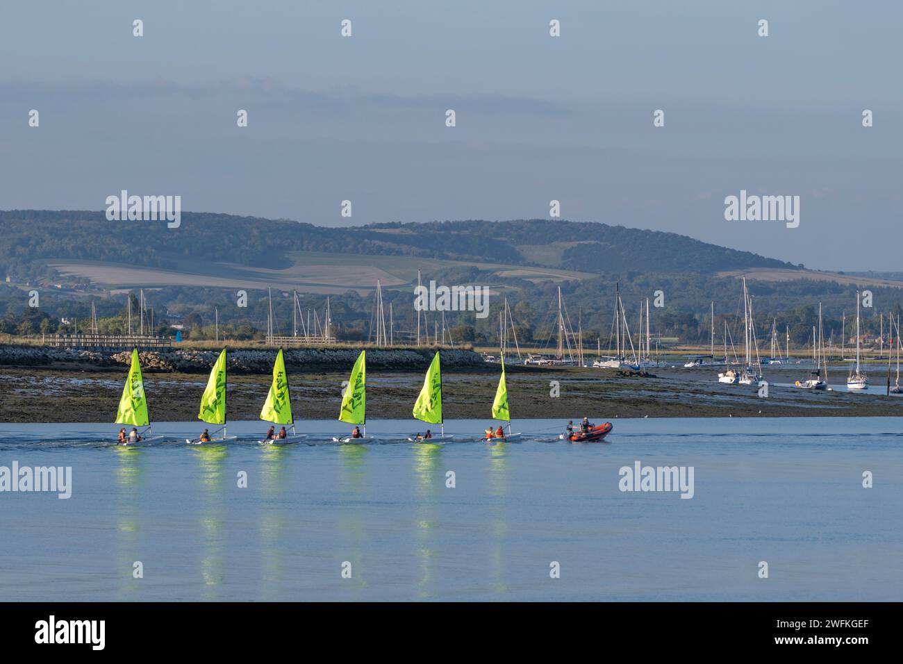 Youngsters on their sailing dingies being towed by an RIB at low tide in Chichester Harbour with far reaching views of the South Downs Stock Photo