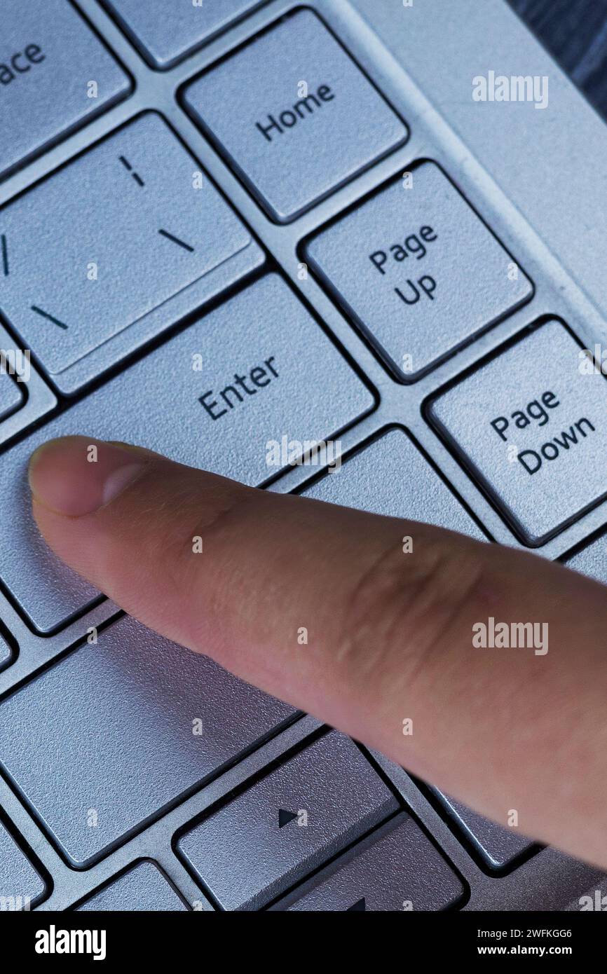Finger pressing an enter key. Computer user hitting the enter key, up close. Confirmation, sending a message Stock Photo