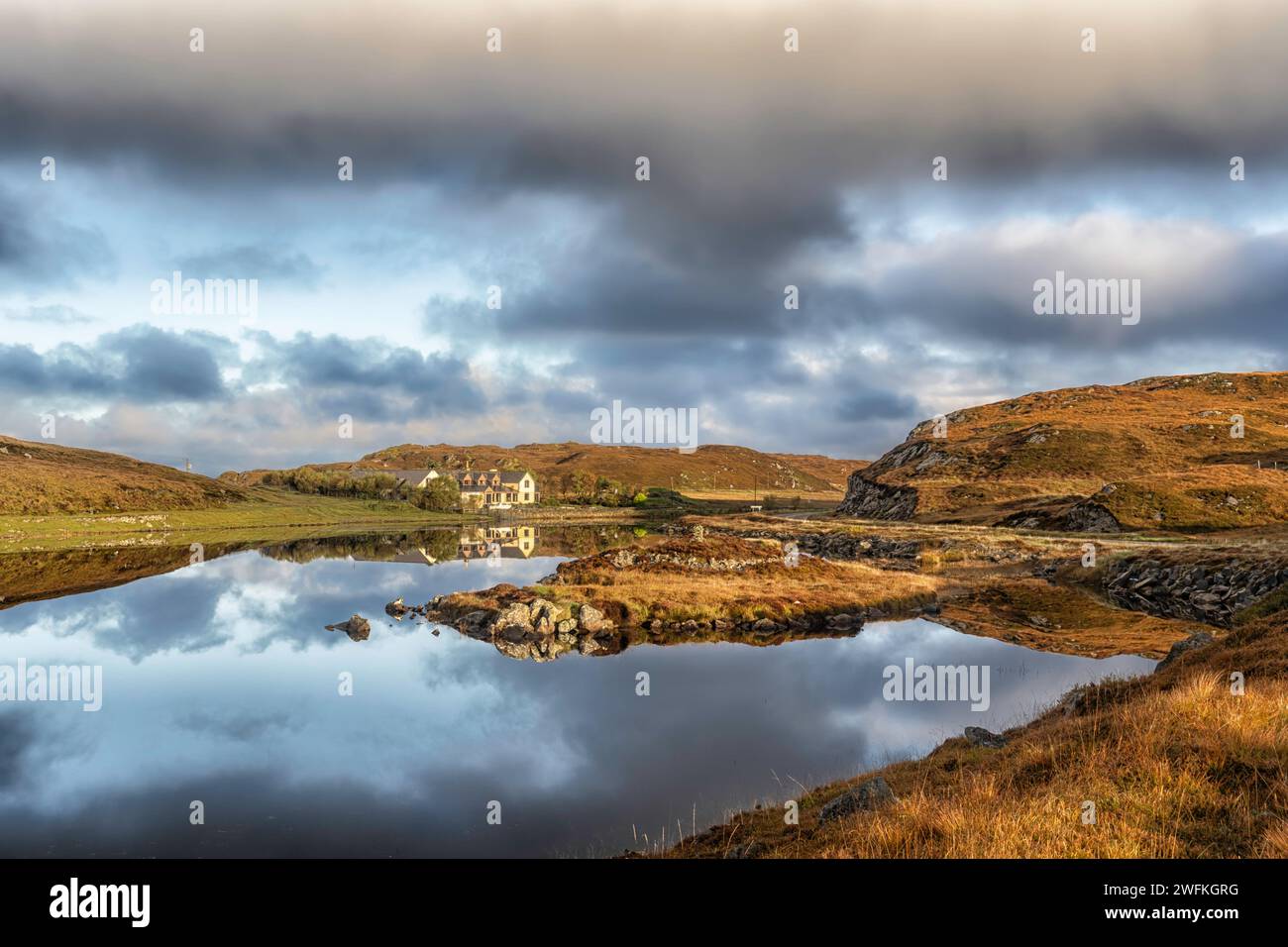 The Doune Braes Hotel in the township of Carloway reflected in the calm and still waters of Loch an Dunain on the Isle of Lewis in the Outer Hebrides. Stock Photo