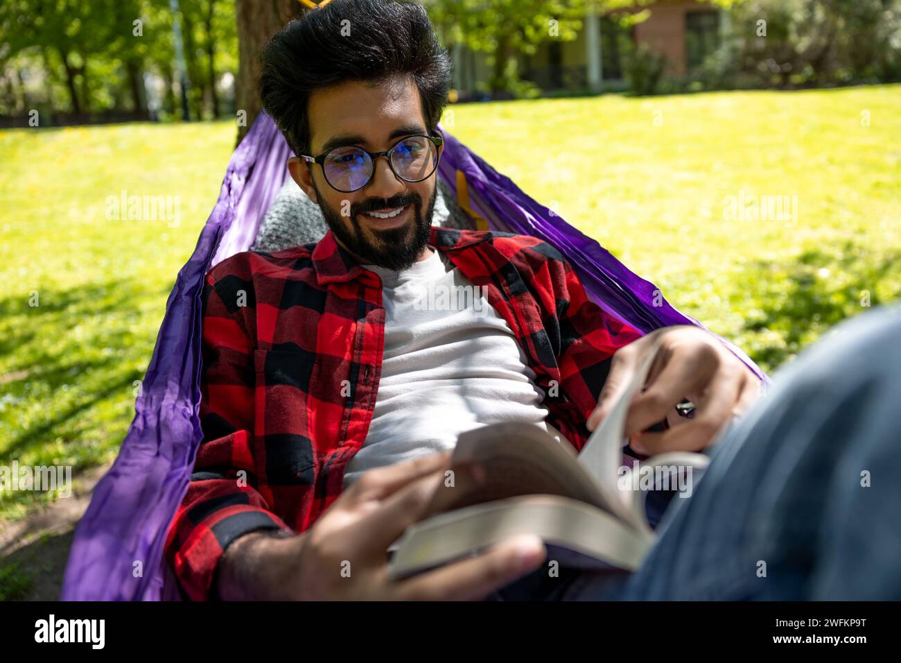 Dark-haired young man reading a book while laying in hammock Stock ...