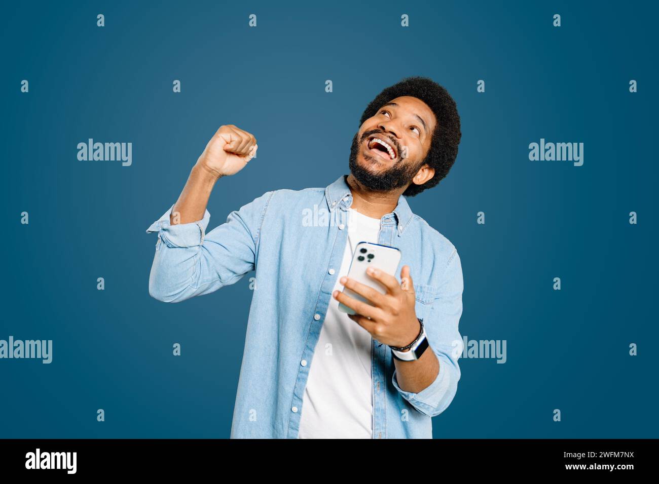 Man is captured in moment of elation, looking upwards and fist pumping air after a successful digital interaction or a win. This portrays a strong emotional response to positive digital communication. Stock Photo