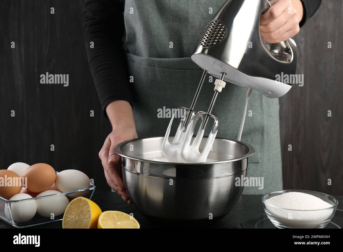 Woman making whipped cream with hand mixer at black table, closeup