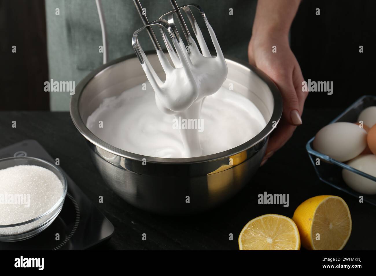Woman making whipped cream with hand mixer at black table, closeup