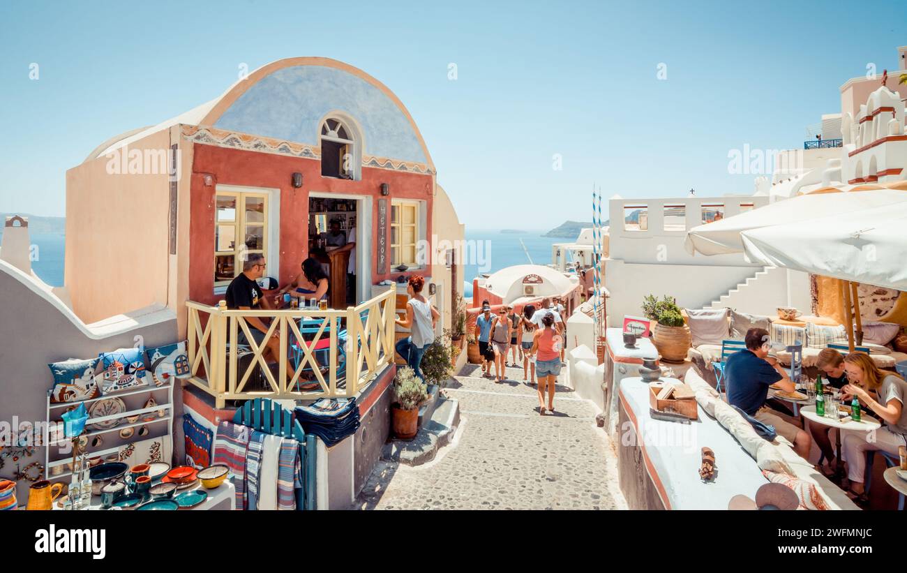 busy tourist street on Santorini island. Oia village with numerous gift shops and cafes; Cyclades islands in the background. Stock Photo