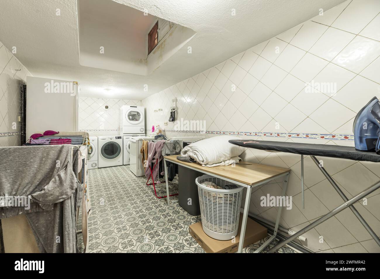 A room dedicated to laundry on the ground floor of a house full of clotheslines full of clothes, washing machines, dryers and ironing utensils Stock Photo