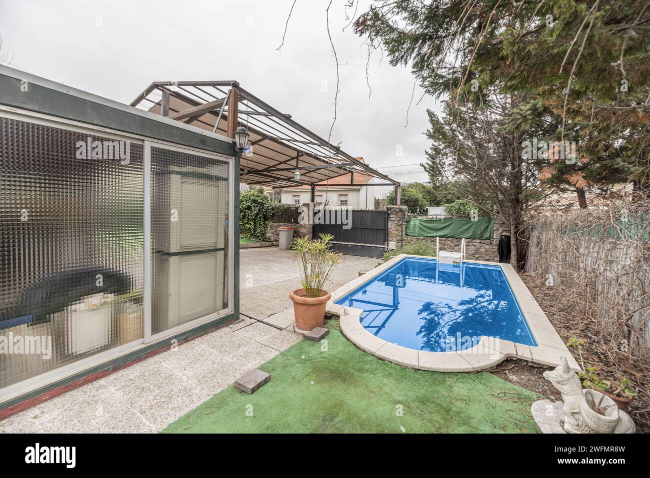 A small pool within a plot with a large awning on a metal structure and a porch with an aluminum and glass enclosure. Stock Photo