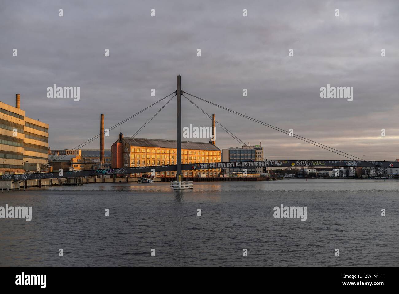 The former KWO (Kabelwerk Oberspree) listed building and the Kaisersteg Brucke in the foreground during sunset, Treptow - Koepenick, Berlin, Germany Stock Photo