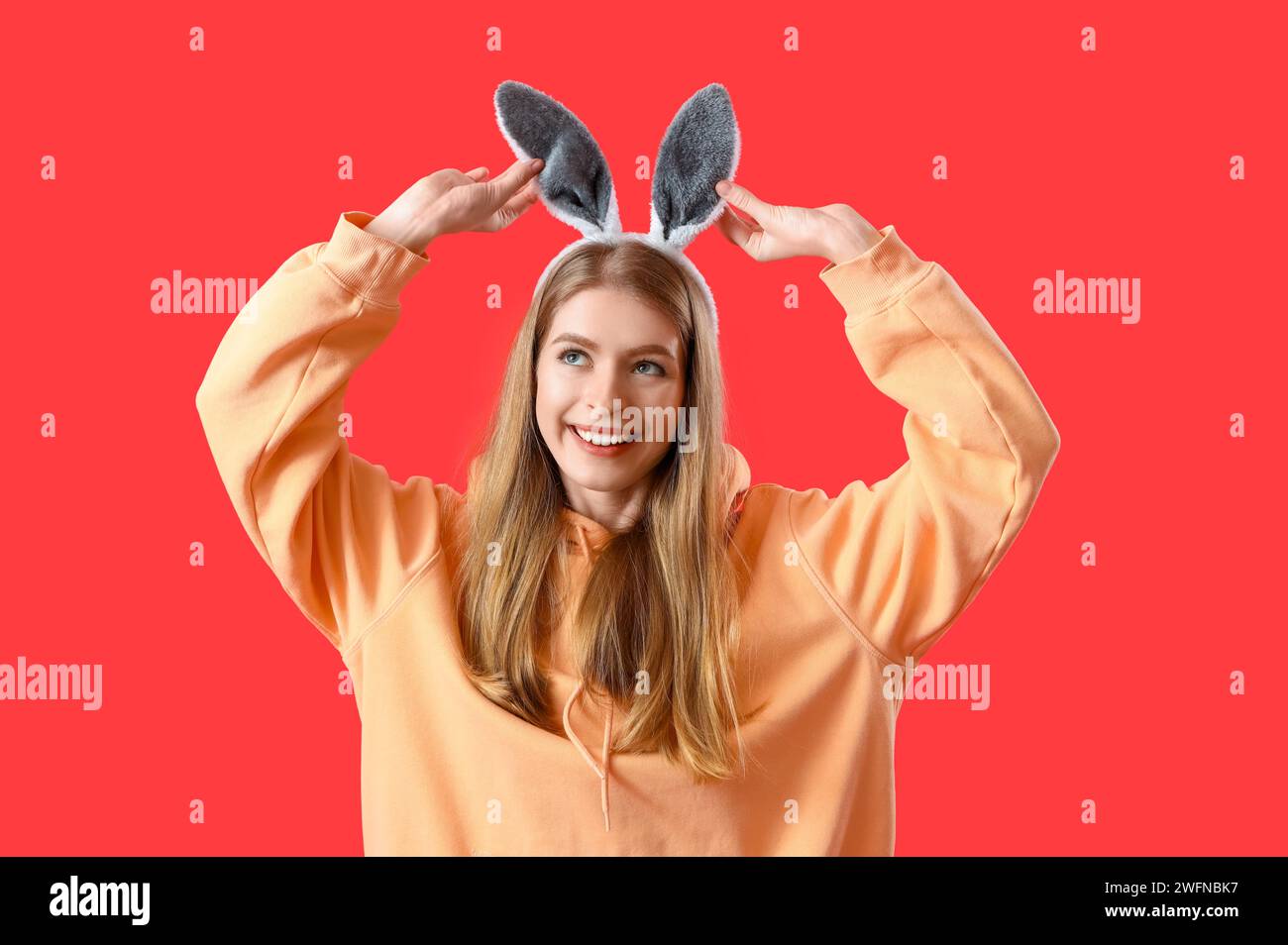 Young woman in bunny ears on red background. Easter celebration Stock Photo