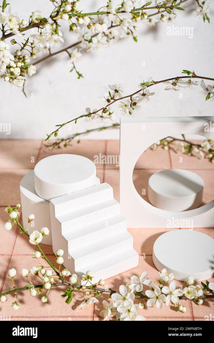 Podiums with blooming branches on table near white wall. Hello spring ...