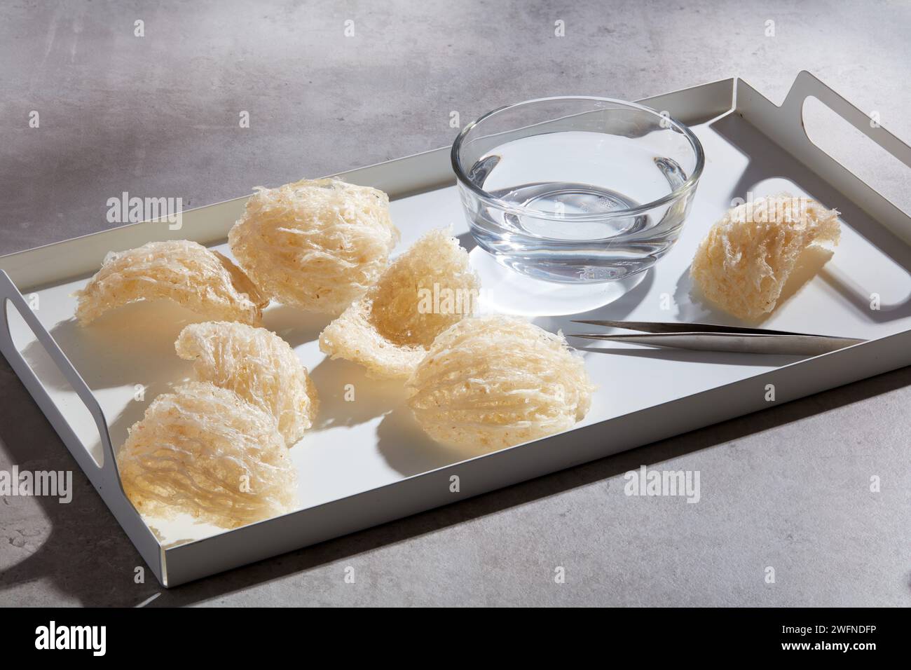 Edible bird nest, a glass transparent bowl of water and a tweezers