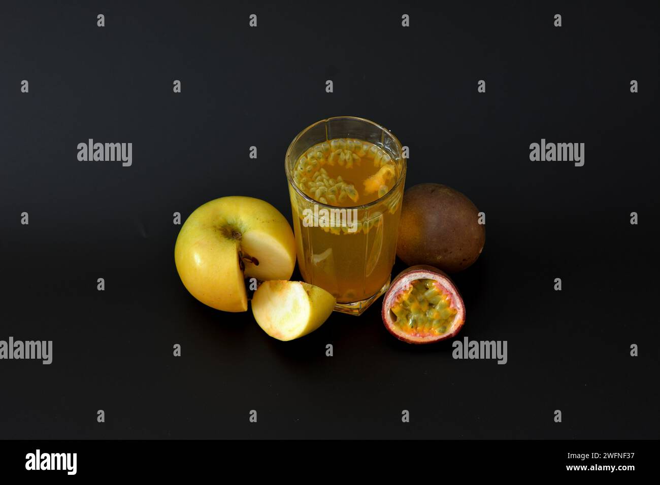 A glass of fruit juice with seeds on a black background, next to pieces of ripe passion fruit and a green apple, Top view, flat lay. Stock Photo